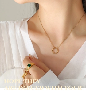 Détail du collier pendentif anneau torsadé et bague émeraude sur mannequin en blanc