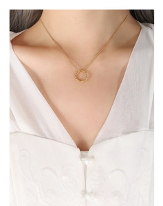 Détail du collier en maille torsadée dorée sur mannequin en tenue blanche brodée