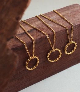 Gros plan de trois colliers dorés avec pendentifs cercles torsadés sur socle en bois