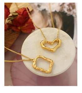 Macro shot of gold heart and square hammered pendants on white marble display stand