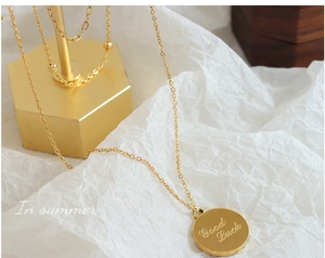 Detail shot of a round gold pendant engraved with Good Luck on a thin metal chain