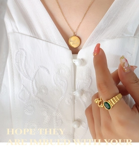 Detail of 18K gold-plated necklace with Good Luck pendant and green gemstone ring