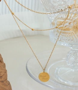 Detailed macro view of layered gold necklace with engraved Good Luck coin pendant