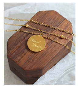 Close-up of gold layered necklace with Good Luck coin pendant on hexagon wood box