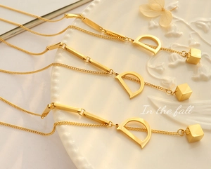 Detail of 18K gold plated D-letter pendant and mini cube charm on fine link chain
