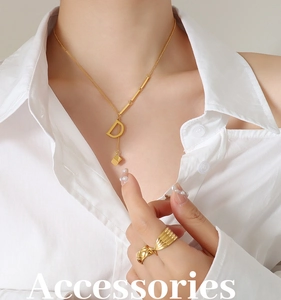 Detail of gold D-pendant necklace and woven wave ring worn with a white shirt