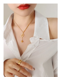 Detail of 18K gold-plated D-letter pendant necklace and stacked rings on a model