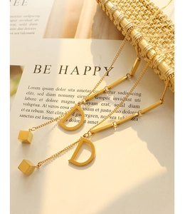 Detail of 18K gold-plated D-letter square pendant with sleek tassels and metallic finish