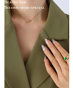 Detail of minimalist gold bead necklace and oval green gemstone ring on a female model