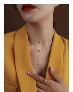 Detail of layered gold beaded necklace and ribbed ring worn with a yellow blazer