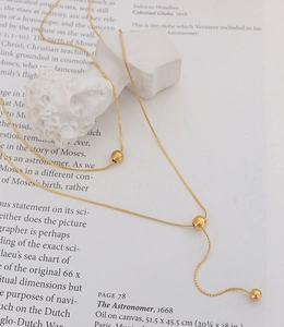 Detailed view of elegant double-layered gold Y-shaped necklace with polished beads on a book