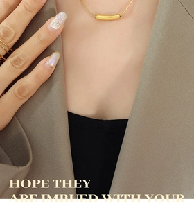 Detail of a minimalist gold snake chain necklace with a smooth cylinder pendant on a model