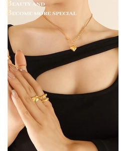 Close-up of gold 3D heart necklace and stacked textured rings on model wearing black