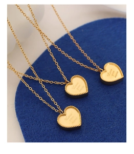 Gros plan détaillé de trois pendentifs cœur dorés avec gravure Love You More sur feutre