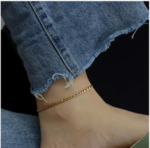 Close-up of golden Figaro chain anklet on ankle paired with denim blue jeans