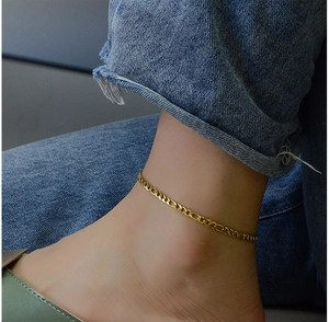 Close-up of a vintage chunky gold chain anklet worn with denim jeans for a stylish look