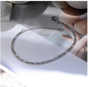 Detailed view of silver Figaro chain anklet with lobster clasp and oval logo tag