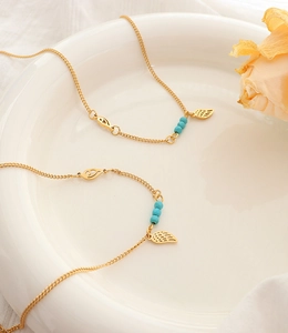 Détail de bracelet de cheville doré en titane avec perles turquoise et breloques plumes