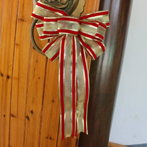 Large handmade Christmas bow with red and gold stripes hanging on a wooden door handle