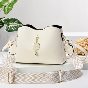 Beige faux leather handbag with golden cat pendant and decorative woven strap on stand