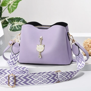 Detail of lavender textured handbag featuring a golden cat pendant and geometric woven strap