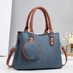 Sac à main bleu à motif crocodile avec poignées marron et un pendentif porte-monnaie rond