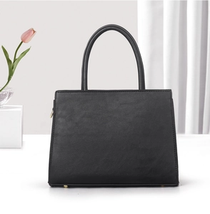 Detail view of black matte leather handbag with gold zipper and flat base on white surface