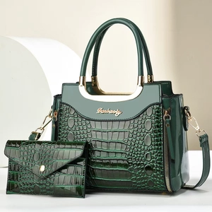 Detail of dark green crocodile pattern patent leather handbag set with gold handles