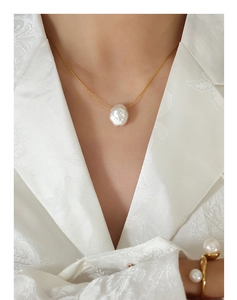 Dettaglio del pendente con perla barocca su catena dorata con blazer bianco