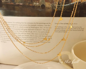 Detail of layered gold heart necklace showing polished charms on a warm magazine background