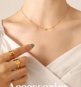 Close-up of golden necklace with three heart pendants and textured gold rings on hand