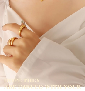 Detailed view of minimalist gold heart necklace and twisted rope ring worn by model
