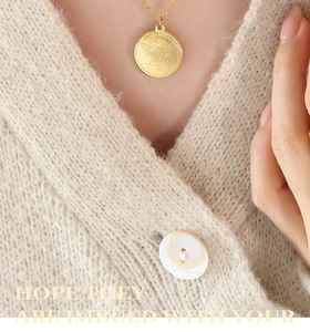 Dettaglio della collana con ciondolo angelo cupido placcato oro su maglione beige