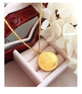 Dettaglio della collana con ciondolo a moneta d'oro e angelo su portagioie rosso