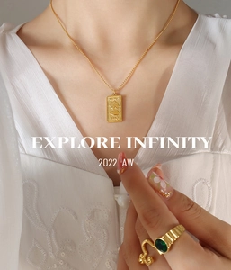 Detail of gold pendant necklace with portrait relief and green gemstone ring on a model