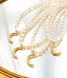 Detail of freshwater baroque pearl necklaces with hammered gold moon pendants on a mirror