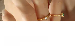 Detail of elegant gold-plated ring set with white zircon and green emerald stones