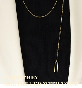 Gros plan d'un collier long doré minimaliste avec un pendentif rectangulaire géométrique