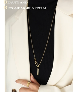 Détail du collier à maillons géométriques dorés et bague sur pull noir et blazer crème