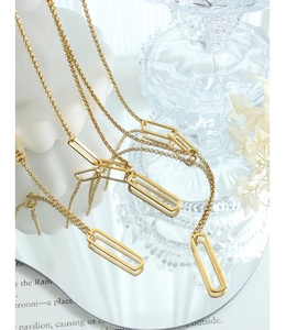 Réflexion artistique d'un collier minimaliste à pendentif rectangulaire doré sur miroir