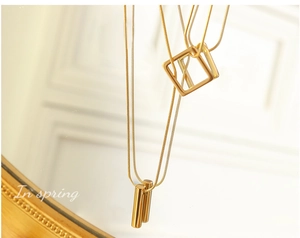 Detail of layered gold geometric square and bar pendant necklaces on snake chains