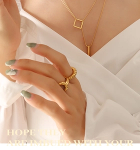 Detail of layered gold geometric necklace and textured spiral ring on a female model