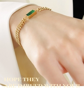 Detail of gold double-layer chain bracelet with emerald-cut green stone on wrist