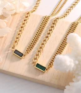 Detail of gold chunky Cuban chain necklaces with black and green emerald-cut gemstones