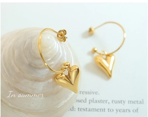 Détail de boucles d'oreilles pendantes en forme de cœur doré sur un coquillage blanc