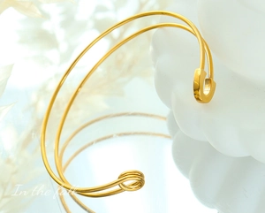 Macro shot of gold safety pin bangle with dual coil design and mirror reflection