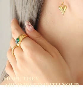 Gros plan d'une bague dorée avec pierre verte et boucles d'oreilles cœur en or