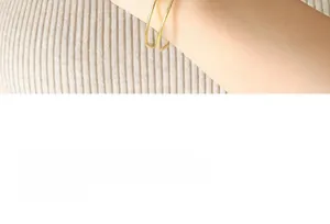 Detail of minimalist gold safety pin bracelets and rings set on female model's wrist