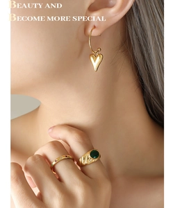 Gros plan de boucles d'oreilles cœur dorées et bagues émeraude vintage sur un mannequin