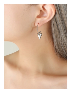 Gros plan de boucles d'oreilles cœur en argent poli portées par un mannequin en vue latérale